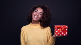Young happy young indian woman pointing finger at a present box with red ribbon isolated over black