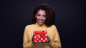 Smiling happy young indian woman giving a present box with red ribbon isolated over black