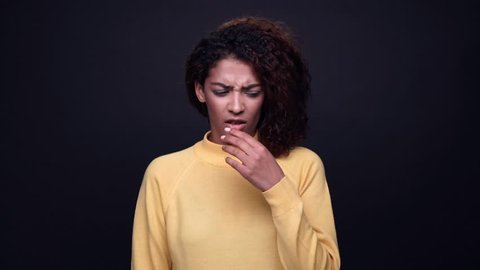 Unhappy young indian woman covers her nose because of bad smell isolated over black 
