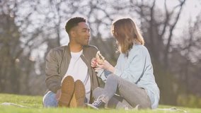 Happy laughing couple sitting in park and eating croissant