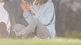 Happy young couple sitting in park and eating croissant
