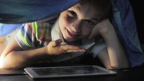 Boy lying under blanket and watching cartoon on touch pad