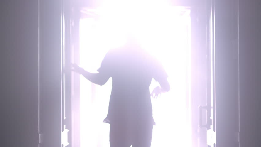 Man silhouette back going to the light at night. Male silhouette going to bright light. Man silhouette walking to light in the darkness. Man open door light in dark. Escape concept