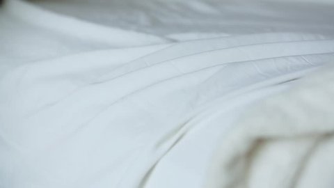 A short clip of a woman's hand smoothing over a white bed sheet to tidy it. Shot in slow motion.