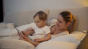 4k video of cute smiling baby boy watching cartoons on tablet with mother in bed