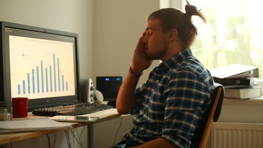 Young man sitting in fron of the computer and looks very tired
