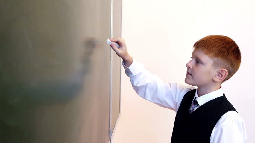 Serious schoolboy writing physical formula on the blackboard