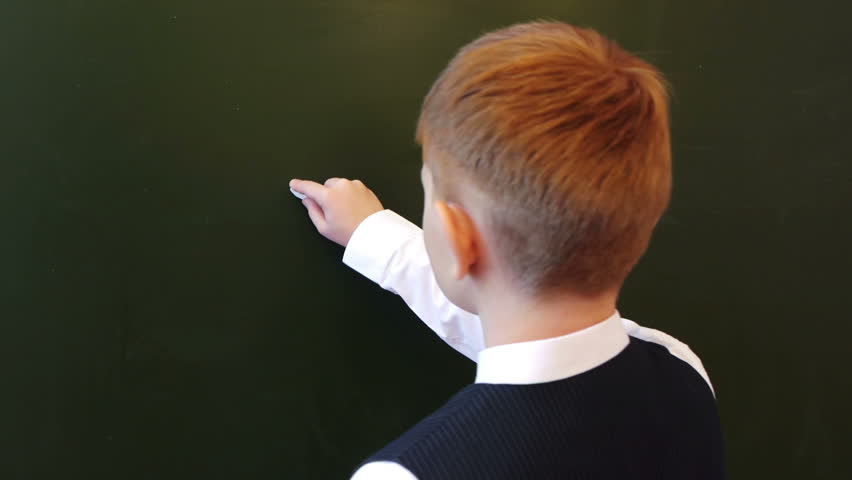 Schoolboy writing physical formula on the blackboard in the school