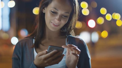Attractive Woman using Mobile Phone During Walk on Streets of Night Town. 