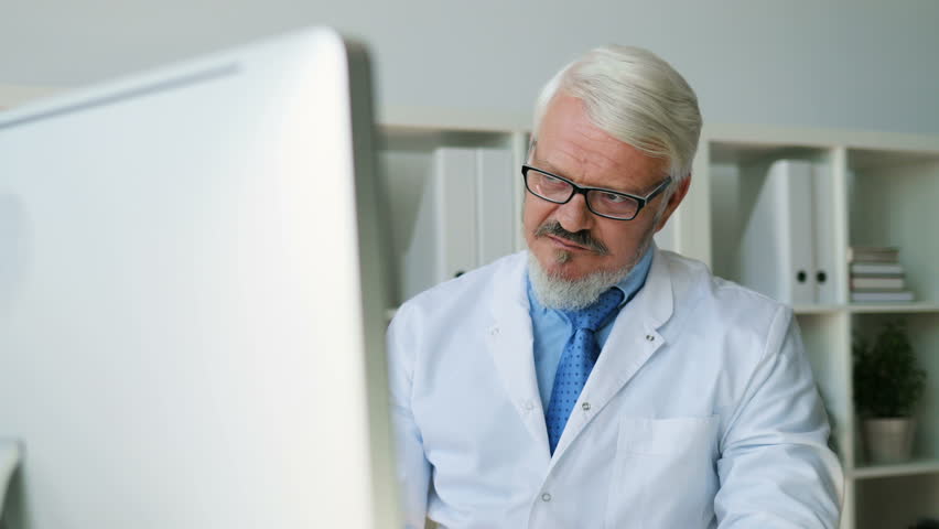 Caucasian young female doctor coming to office of midle aged male doctor and talking about something looked on tablet. Indoor.