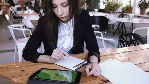 Businesswoman using tablet computer with green touch screen in cafe. Young beautiful student reads a tablet and make notepads in a notepad sitting in a loft cafe, a wooden table.background of a cafe.