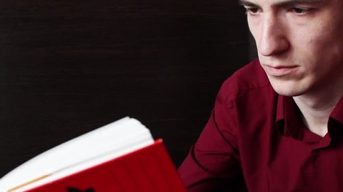 A young guy in a red shirt calmly reads a red book