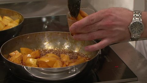 DUBAI, UAE - CIRCA 2013: CU of a male chef's hands scooping caramelised mangoes from a pan on a stove into a small glass ramekin.
