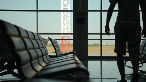 Man come and stand at full height, gaze out airport terminal window, silhouette