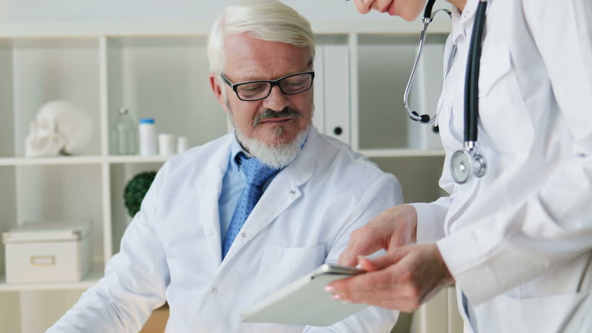 Caucasian young beautiful female doctor and midle aged male doctor in glasses using tablet. Indoor.