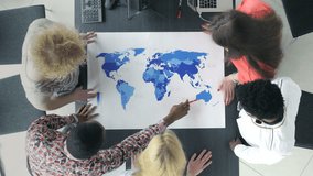 Young office workers discussing the business possibilities worldwide. View from above of business people studying the world map. - Powered by Shutterstock - Get 15% off with code: PIKWIZARD15