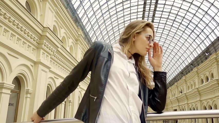 Young beautiful girl with long blond hair in a shiny leather jacket takes off his glasses and looks away. Walk around the old town.