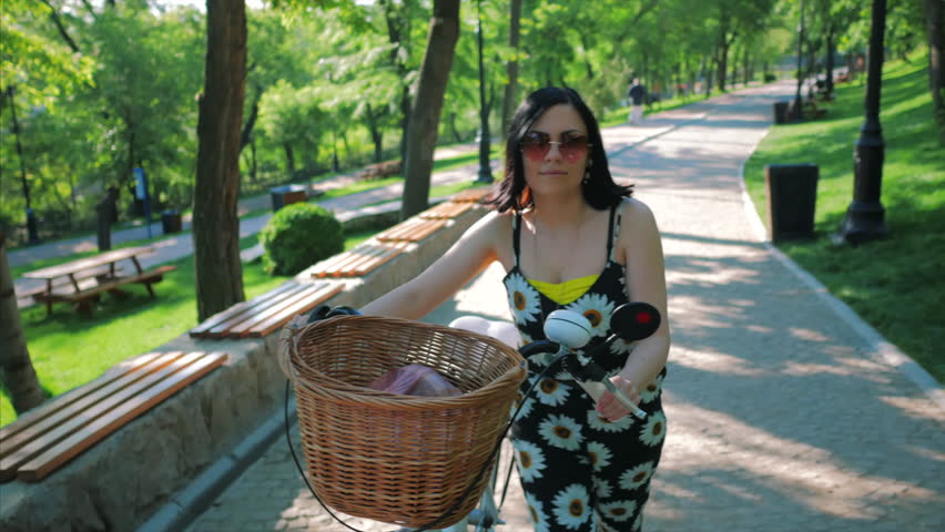 woman walk in the spring park by bicycle and climbs the small hill. Girl walking with vintage white bike near the trees at beautiful sunrise on green front. 4k
