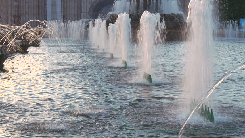 Beautiful fountain in the city park. The sun illuminates the splashes of water. Shining splash of water.