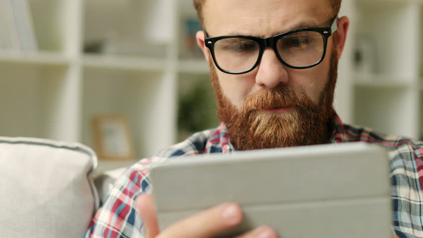 Man with beard with smartphone sitting on sofa at home in the living room and chatting with friends. Close up.