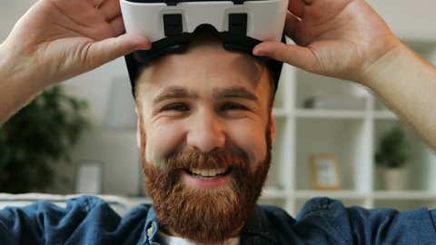Young hipster man using his VR headset for watching the 360 video while sitting on sofa at home in the living room. Close up. Stockvideo