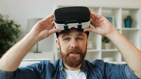 Caucasian hipster man in casual shirt using his VR headset at home in the living room. Close up.