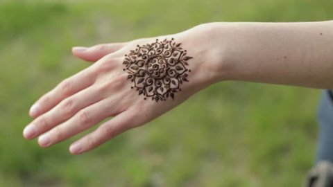 Hand of young caucasian woman with floral mehndi tattoo. Close up shot. Blurry nature background.