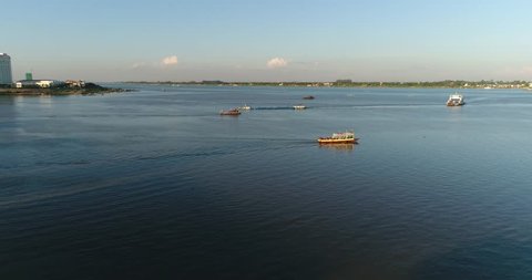 Drone footage of the center of Phnom Penh where the Mekong river meets the Tonle Sap river. Shot over the water around sunset time showing car ferry, fishing, tourist and transport boats on the river.
