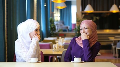 Two beautiful young Muslim women in a cafe communicate and laugh