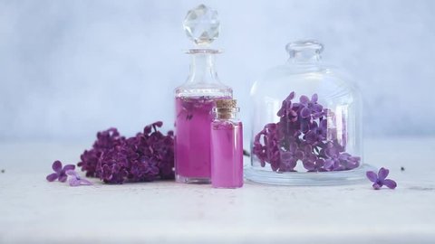 Someone hand placing lilac essence in glass vial, with fresh lilac flowers