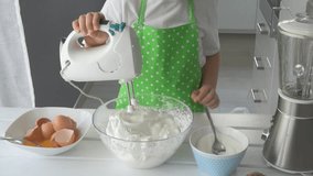 Slow motion video of child mixing cream for cake with electric mixer. Boy prepares a delicious dessert - meringue