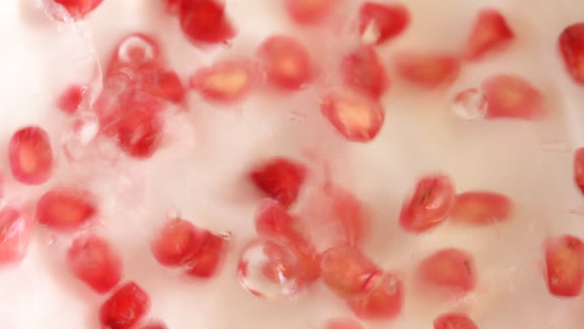 Ripe pomegranate seeds falling into water.