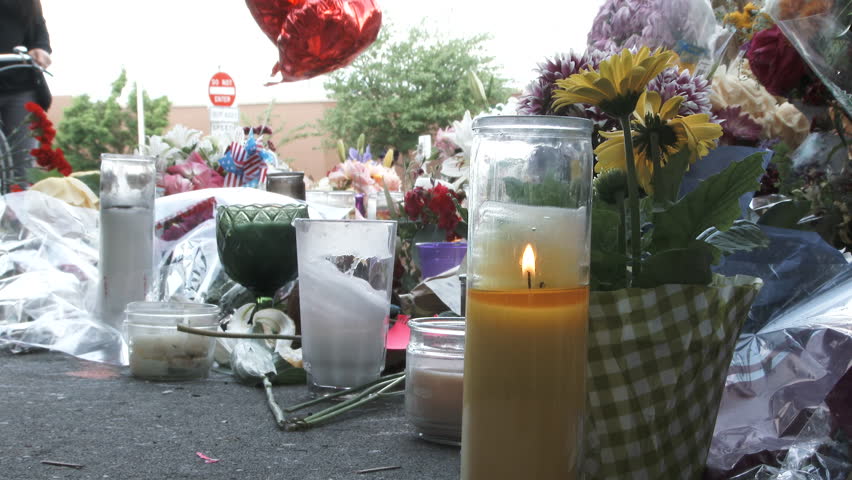 Unrecognizable people walk by flowers, balloons, candles and other offerings at memorial for victims of a hate crime in Portland, Oregon.