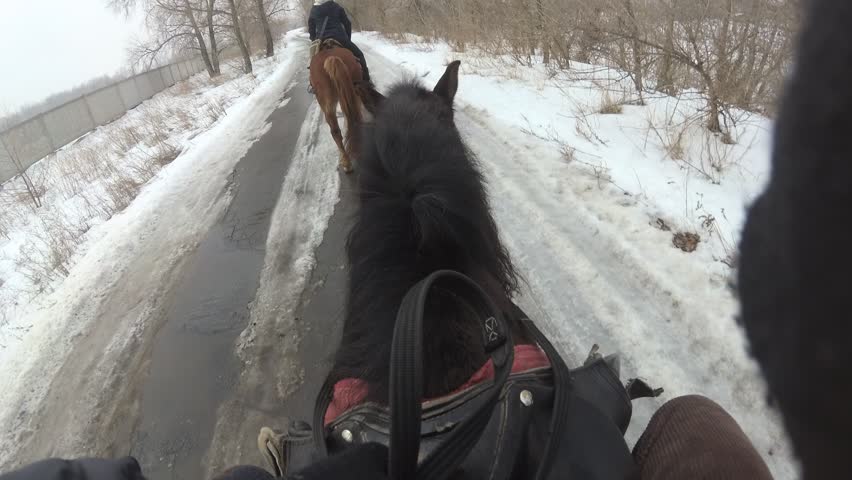Riding a black horse in winter with a snowy landscape. First person view, top view