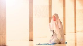 Video footage of a young female muslim wearing a prayer veil and praying in the mosque while sitting and raising her hands