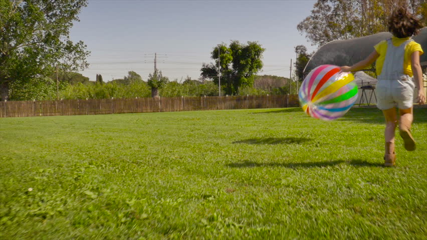 Little girl running after with big coloroful jumbo ball the the farm