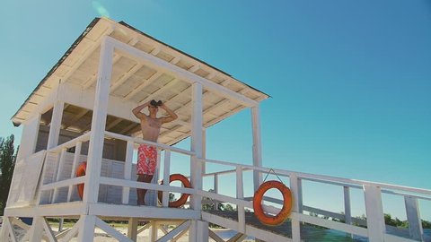 Lifeguard on the beach looks through binoculars and notices the person in need of help. He rushes to his aid, jumping over the fence. Slow Motion 120fps