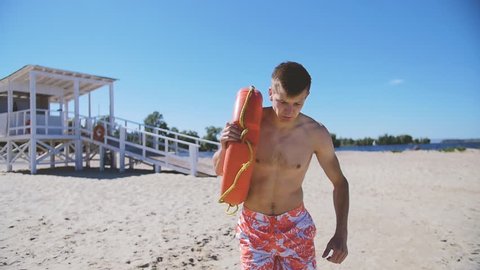 A beach lifeguard with a bare torso runs along the beach to help a drowned man. In slow motion.