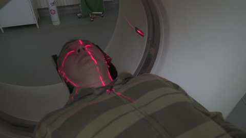 Middle aged man lying on the CT or MRI scanner during machine imaging his body, lights up infrared rays and male patient passes through the circle, crane shot from portrait to up, room interior