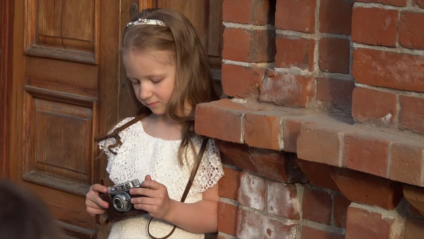 The girl in a pink dress considers the old camera in hands