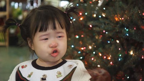 Beautiful baby asian toddler girl in front of Christmas tree pouting