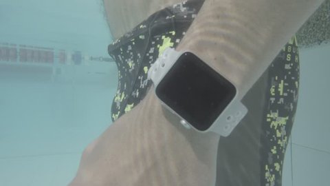 Underwater CU of swimmer checking his digital watch. Camera comes to surface with hand movement