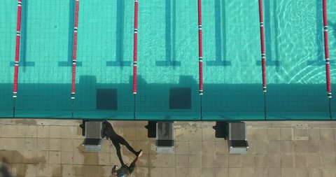 Drone bird's eye view of swimmer jumping into pool; trailing him