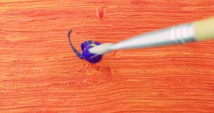 Very close video of painting with blue acrylic paint over orange with a small paintbrush.