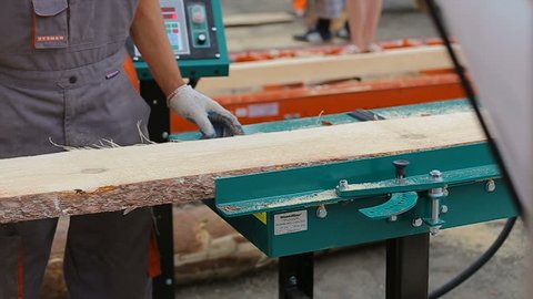 Workers loads boards onto trimming machine from pile. Industrial edger multirip trims boards