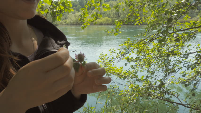 Young Woman Tears Off Petals of a Flower by the River
