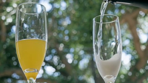 Prosecco pours into a champagne flute at an outdoor bar. A glass of orange juice sits nearby to make mimosas. The alcoholic beverage is typically served during Sunday brunch  as a bottomless option.