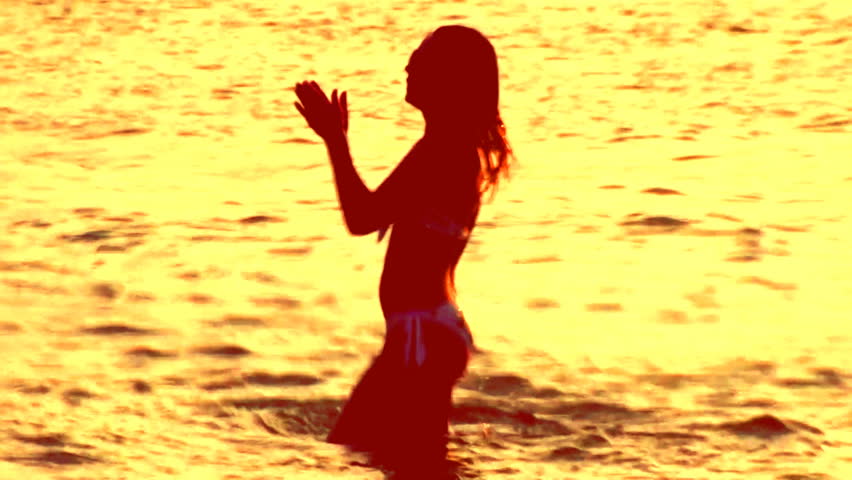 women in shadow as she dances in the sea at sunset