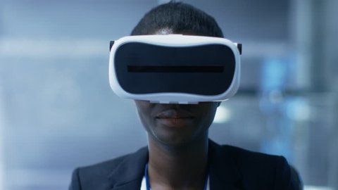 Young Black Female Virtual Reality Engineer Developer Wearing VR Headset Creates Content. She's Alone in a Modern Laboratory Research Center. Shot on RED EPIC-W 8K Helium Cinema Camera.