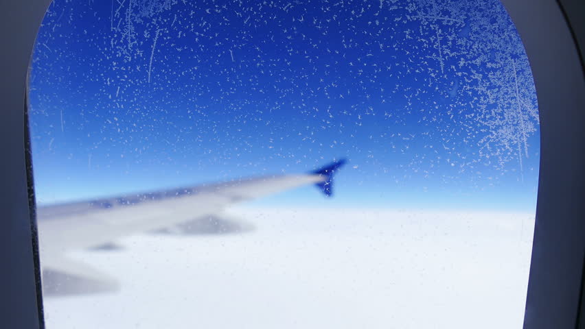 Travel concept: tilt up of hoarfrost on the aircraft window on the background of blue sky.
